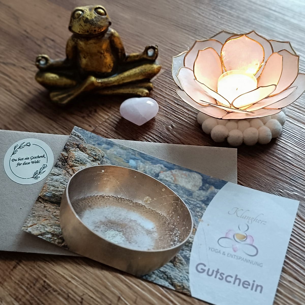 Vorderseite der Klangherz-Gutschein-Karte mit Klangschalen-Motiv und Klangherz-Logo, daneben Meditationsfrosch, Lotus-Teelicht und Rosenquarz-Herz