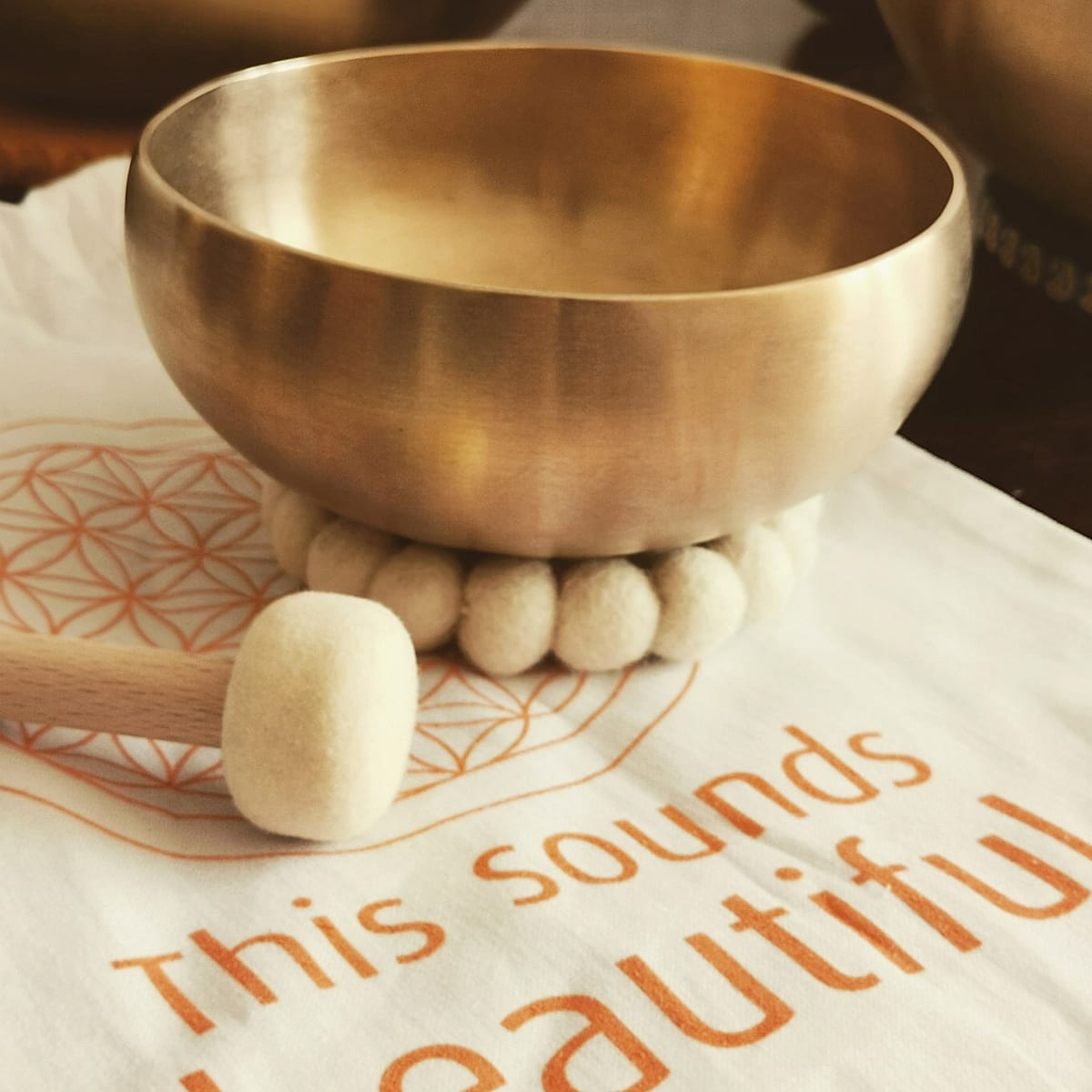Goldene Klangschale mit Filzklöppel auf einem hellen Tuch mit dem Schriftzug „This sounds beautiful“