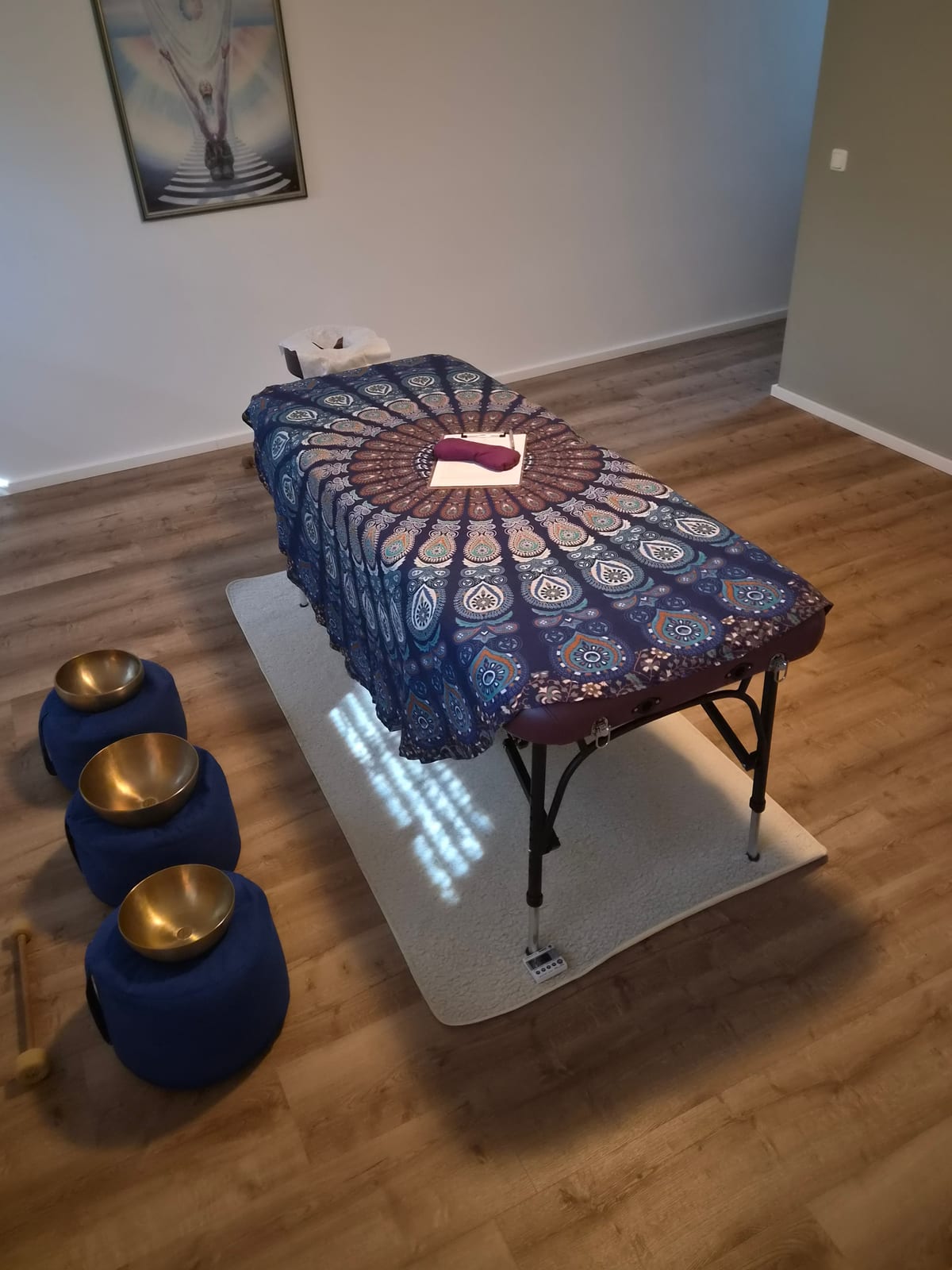 Blick in den Raum: Massageliege mit aufgestellten Klangschalen, warmes Licht, ruhige Atmosphäre