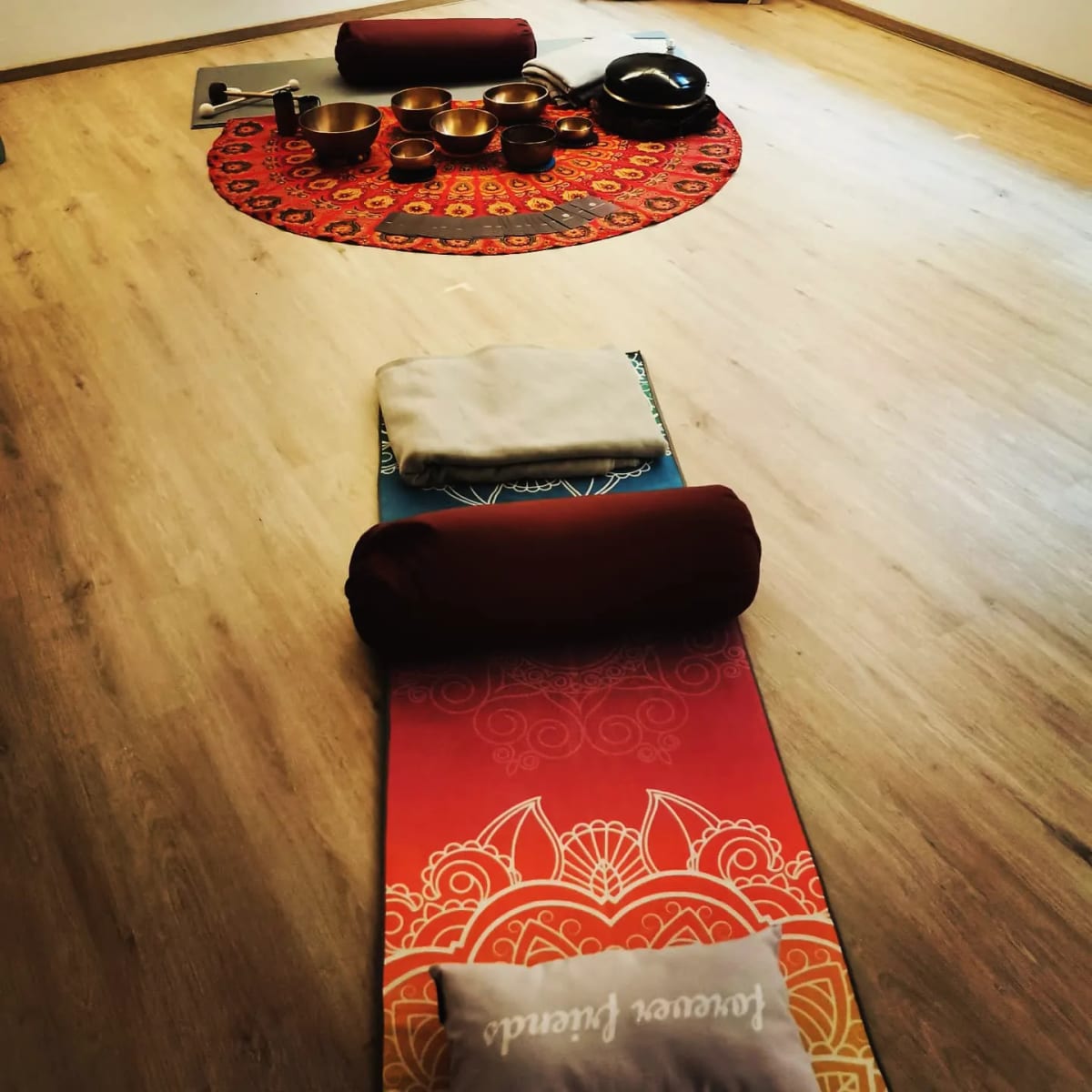 Yogamatten mit Bolstern und ein Kreis aus Klangschalen auf rundem Tuch, vorbereitet für ein Klangbad