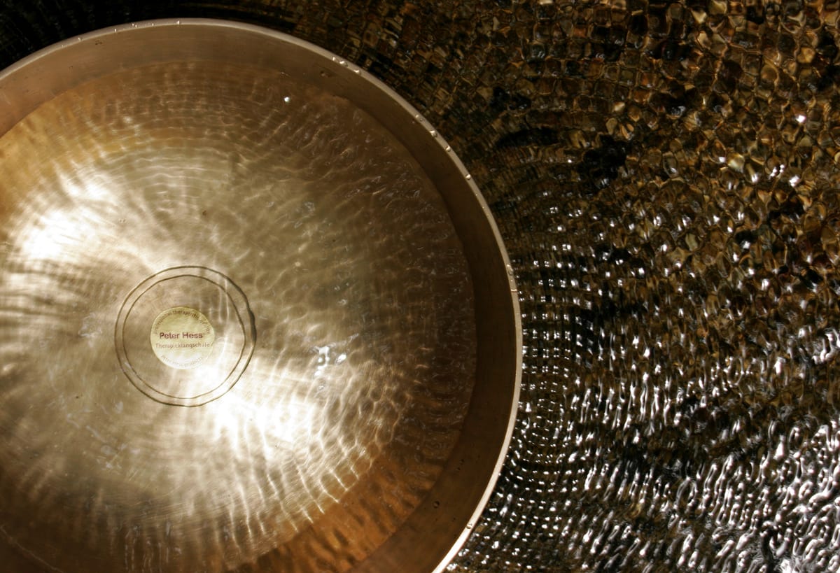 Klangschale, deren Schwingung auf der Wasseroberfläche sichtbar wird. Sinnbild für Klang Yoga